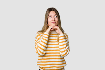 Young blonde posing for a portrait isolated, exuding natural beauty and radiance keeps hands under chin, is looking happily aside.