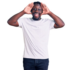Fototapeta na wymiar Young african american man with braids wearing casual white tshirt smiling cheerful playing peek a boo with hands showing face. surprised and exited