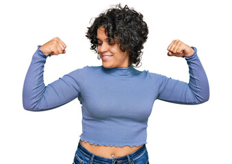 Young hispanic woman with curly hair wearing casual clothes showing arms muscles smiling proud. fitness concept.