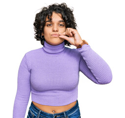 Young hispanic woman with curly hair wearing casual clothes mouth and lips shut as zip with...