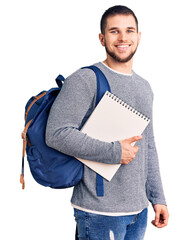 Young handsome man wearing student backpack holding notebook looking positive and happy standing and smiling with a confident smile showing teeth - obrazy, fototapety, plakaty