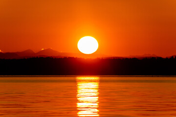 Orange Sun Setting Over Horizon and Mountains Reflecting Off of Strait of Georgia in Vancouver Island , British Columbia, Canada