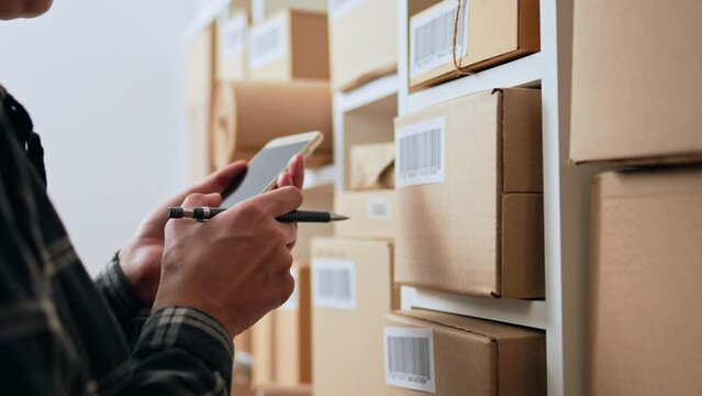Entrepreneurial activity, Courier service entrepreneur holding a smartphone in the premises of a courier company. The packer of the goods organizes the transportation of goods, unpacking
