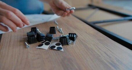 Woman examines set of fittings for assembling furniture in package. Close-up shot