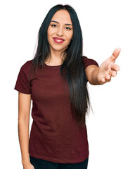 Young hispanic girl wearing casual t shirt smiling friendly offering handshake as greeting and...
