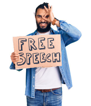 Young arab man holding free speech banner smiling happy doing ok sign with hand on eye looking through fingers