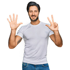 Young hispanic man wearing casual white t shirt showing and pointing up with fingers number eight while smiling confident and happy.