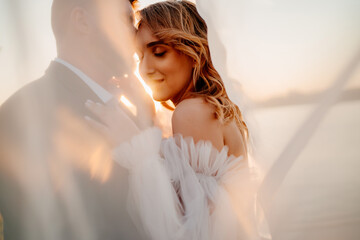 the bride and groom under the veil on the sunset by the river