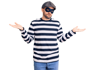 Young handsome man wearing burglar mask clueless and confused expression with arms and hands raised. doubt concept.