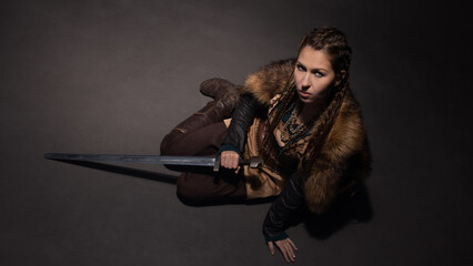 A young brave Viking heroine gazing up sitting on the floor. A young woman in a suit in Scandinavian or fantasy style
