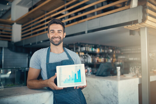 Investing Your Passion Pays Off. Portrait Of A Young Man Holding A Digital Tablet With A Graph On The Screen At A Coffee Shop.