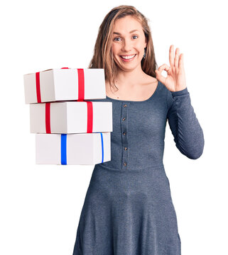 Young beautiful blonde woman holding birthday gift doing ok sign with fingers, smiling friendly gesturing excellent symbol