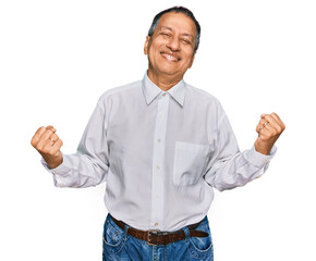 Middle age indian man wearing casual white shirt very happy and excited doing winner gesture with...