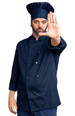 Young hispanic man wearing cooker uniform doing stop sing with palm of the hand. warning expression with negative and serious gesture on the face.