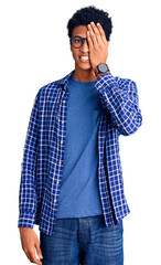 Fototapeta premium Young african american man wearing casual clothes and glasses covering one eye with hand, confident smile on face and surprise emotion.