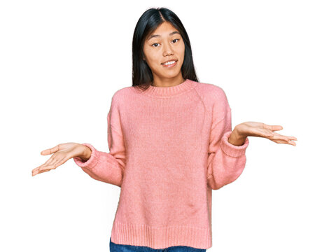 Beautiful young asian woman wearing casual winter sweater clueless and confused expression with arms and hands raised. doubt concept.