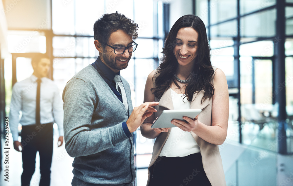 Poster working with twice the expertise. shot of two businesspeople working on a digital tablet in a busy o