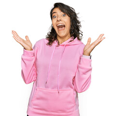 Young hispanic woman wearing casual sweatshirt celebrating crazy and amazed for success with arms raised and open eyes screaming excited. winner concept