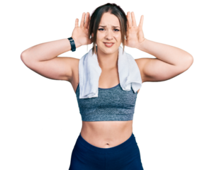 Young hispanic girl wearing sportswear and towel trying to hear both hands on ear gesture, curious for gossip. hearing problem, deaf