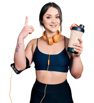 Young hispanic girl wearing sport clothes drinking a protein shake surprised with an idea or question pointing finger with happy face, number one