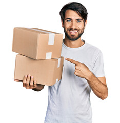 Hispanic man with blue eyes holding packages smiling happy pointing with hand and finger