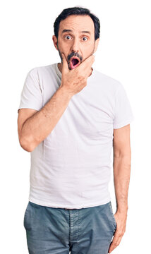 Middle age handsome man wearing casual t-shirt looking fascinated with disbelief, surprise and amazed expression with hands on chin