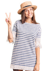 Obraz na płótnie Canvas Beautiful caucasian woman wearing summer hat showing and pointing up with fingers number two while smiling confident and happy.