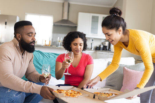 Happy diverse friends sitting on sofa, eating pizza and drinking wine