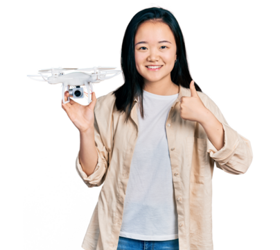 Young chinese woman holding drone smiling happy and positive, thumb up doing excellent and approval sign