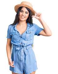 Fototapeta premium Brunette teenager girl wearing summer hat smiling and confident gesturing with hand doing small size sign with fingers looking and the camera. measure concept.