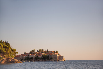 Fototapeta na wymiar Panoramic view of Sveti Stefan in Montenegro at pink sunset. Famous tourist place near Budva. Natural beautiful island, with terracotta roofs among the turquoise sea. Copy space, wallpaper background