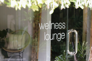 Wellness lounge beauty salon sign on the glass door with greenery reflexion	
