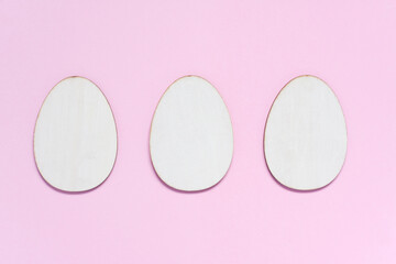 Three flat wooden blanks for creativity in shape of egg on pastel pink background. Happy Easter concept. Mockup for greeting card with space for text. top view, flat lay
