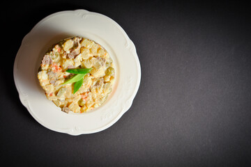 Top view of traditional Russian Olivier salad. Soviet dish served in glass bowl on black background. Salad with green peas, potato, carrot, egg and meat cubes with mayonnaise sauce dressing