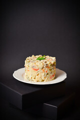 Salad Olivier served in culinary ring with green onion on top located on a black box. Copy space image with space for text with dark background. Soviet Salad with boiled vegetables. Vertical image