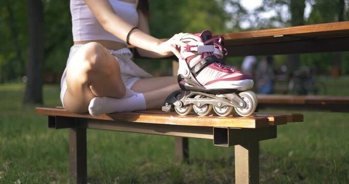 Slim girl sits on a park bench and holds rollerblades in front of her