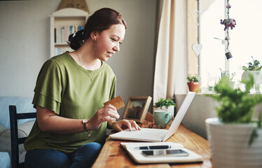 I need to buy this. Cropped shot of an attractive young businesswoman sitting alone in her home office and using her laptop for online shopping.