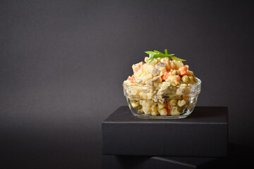 Close up to Traditional Russian salad Olivier served in glass bowl located on box. Salad with...