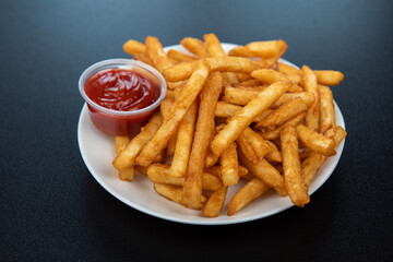 French fries with ketchup on dark background, side view