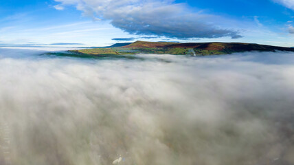 Aerial view flying over a bank of fog over a large large surrounded by mountains (Llangorse Lake, Wales)