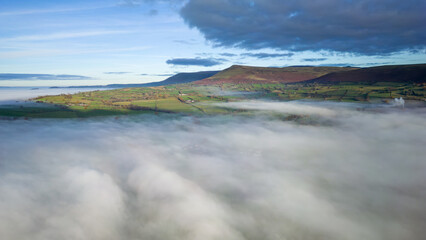 Aerial view flying over a bank of fog over a large large surrounded by mountains (Llangorse Lake, Wales)