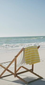 Vertical video of deck chair and towel on beach, in slow motion, with copy space