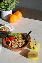 healthy homemade oatmeal in a wooden bowl with fruits on white table