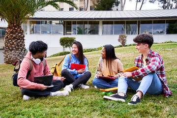 Group portrait of happy teenage students holding notebooks and smiling sitting on courtyard grass...