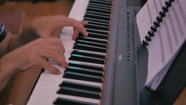 Pianist plays the electric piano during singing rehearsals. Hairy hands press keys of a keyboard piano while looking at the score.