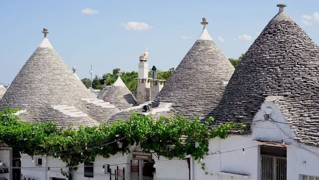 Tourists stroll among Apulian trulli.
Summer holidays in southern Italy. Characteristic trulli houses and people visiting the city on a warm sunny day.