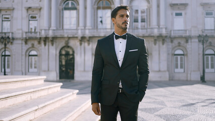 Elegant man in suit stands on street of European city. Action. Attractive man in elegant suit on...