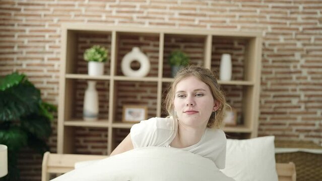 Young blonde woman waking up stretching arms at bedroom