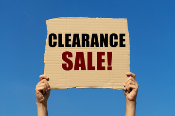 Clearance sale message on box paper held by 2 hands with isolated blue sky background. This message...