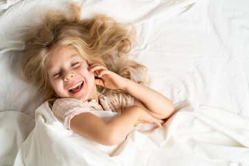 happy little girl in a white bed on a pillow, good morning, healthy baby sleep concept, copy space